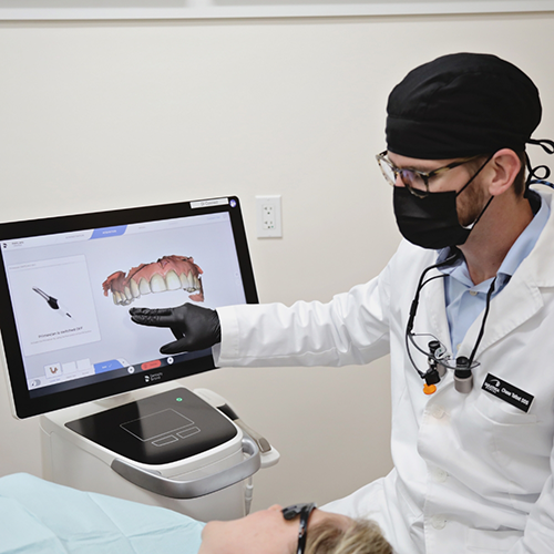 Dentist with mask pointing to image of teeth on monitor