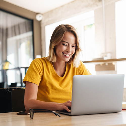 Woman in yellow shirt typing on laptop